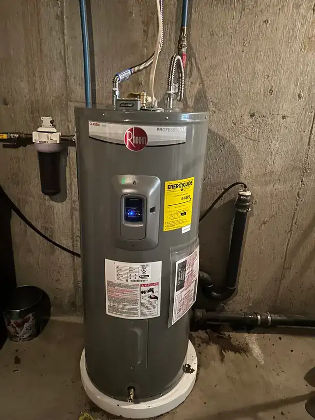 New Rheem electric water heater installed on a stand in a concrete basement