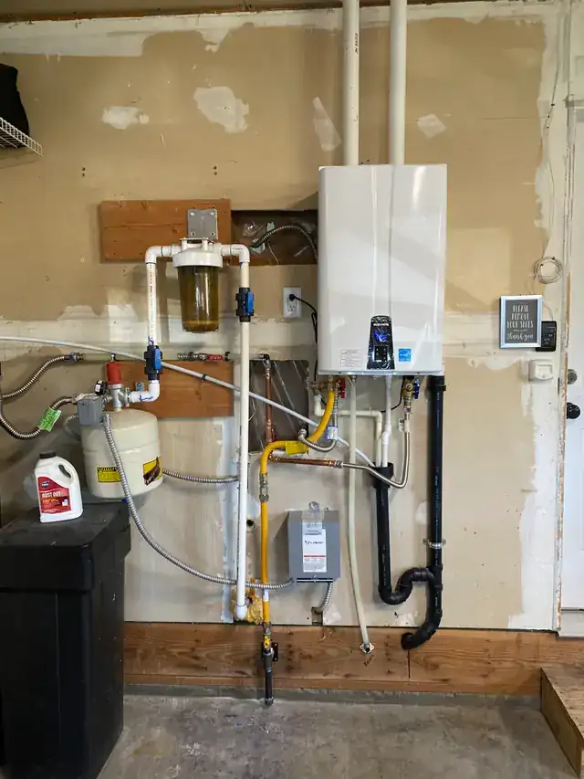 Tankless water heater with a water softener and filter manifold on a garage wall