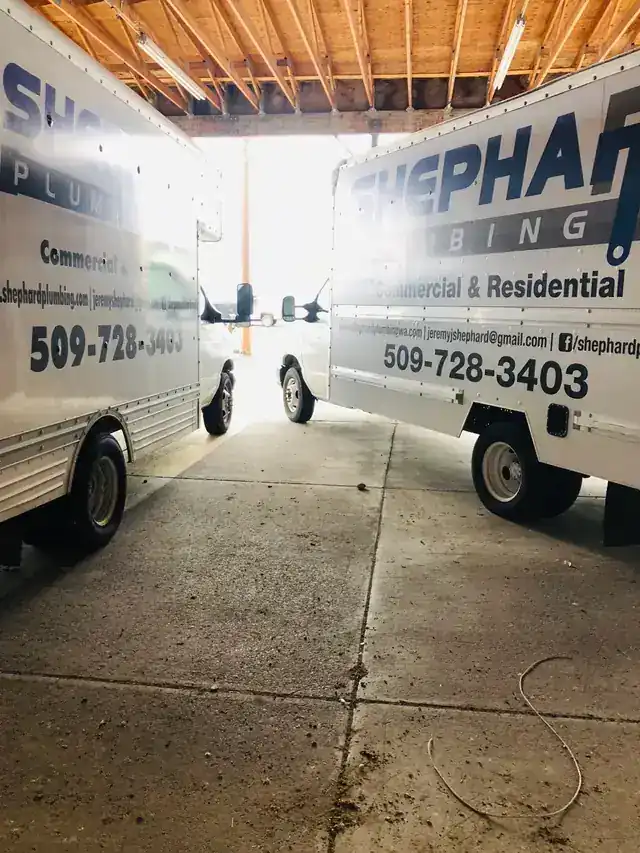 Two lettered box trucks parked nose to nose in the shop bay, backlit
