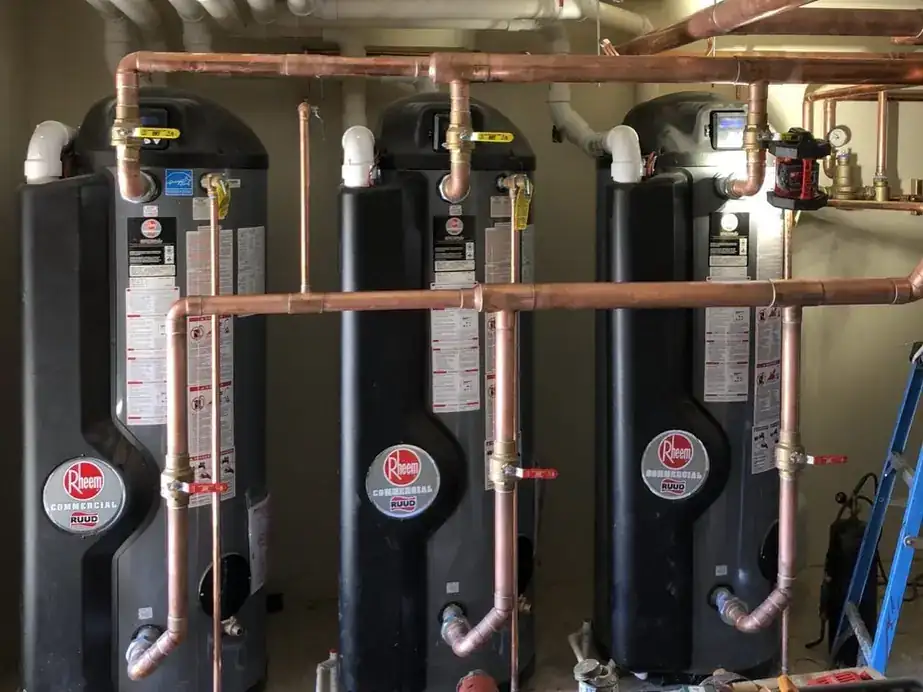 Three Rheem commercial water heaters connected by copper headers with brass valves