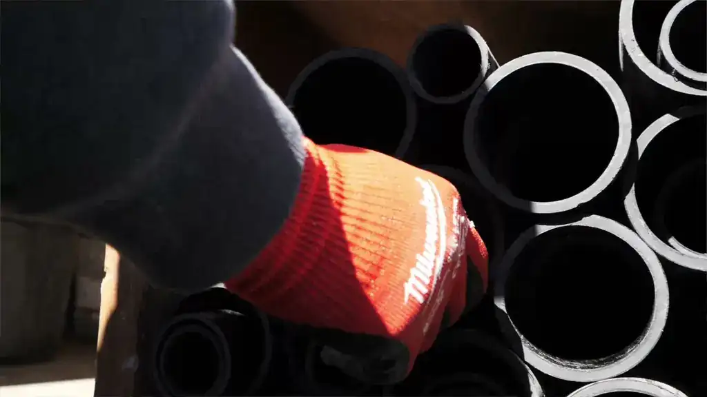 A gloved hand pulling black ABS pipe from a stack