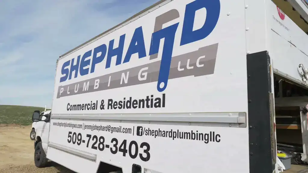 A Shephard box truck parked on open sagebrush ground with a plumber at its side