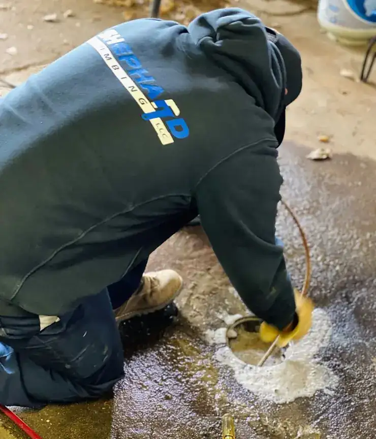 Shephard plumber in a company hoodie working a flooded yard drain