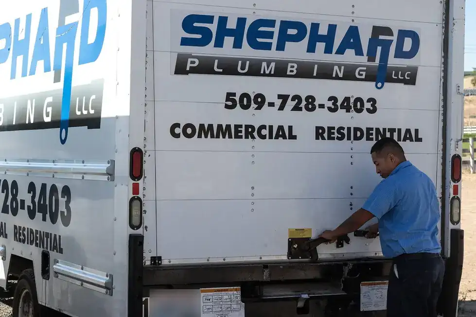 Shephard plumber latching the rear door of a lettered box truck