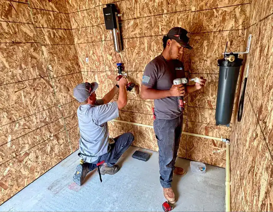 Two plumbers working on a supply manifold mounted on an OSB wall
