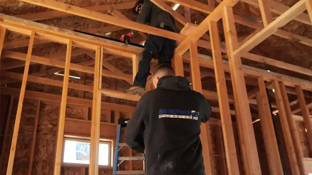 Two Shephard plumbers running pipe through open wall framing on a new build