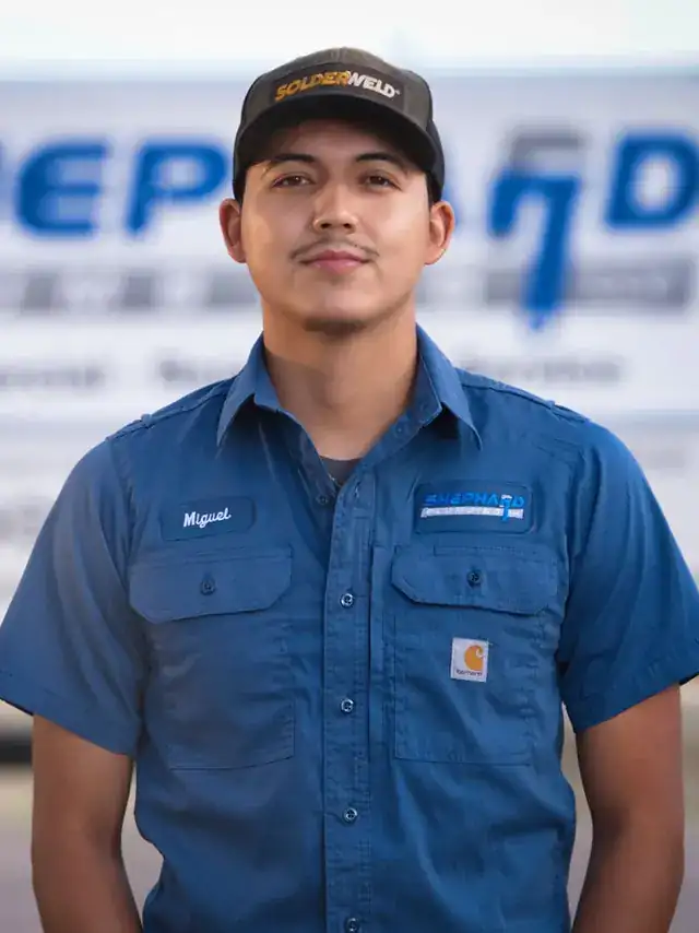 Miguel Torres, Plumber at Shephard Plumbing, in a name-tagged work shirt in front of the box truck