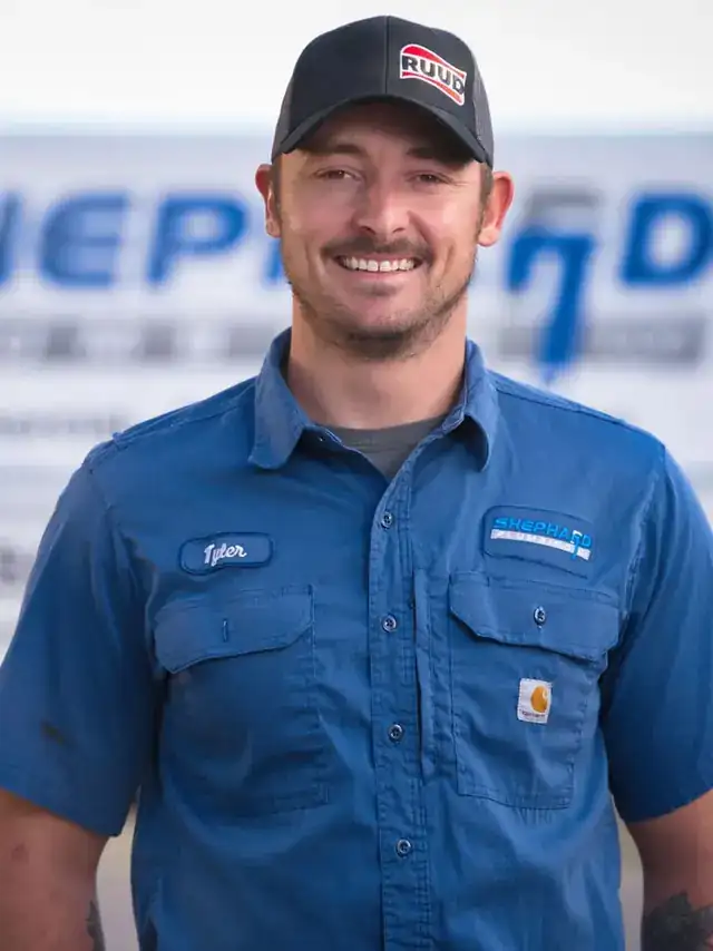 Tyler Hendren, Plumber at Shephard Plumbing, in a name-tagged work shirt in front of the box truck