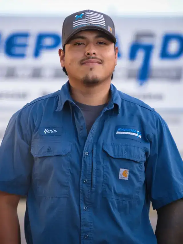 Yahir Cuenca, Plumber at Shephard Plumbing, in a name-tagged work shirt in front of the box truck